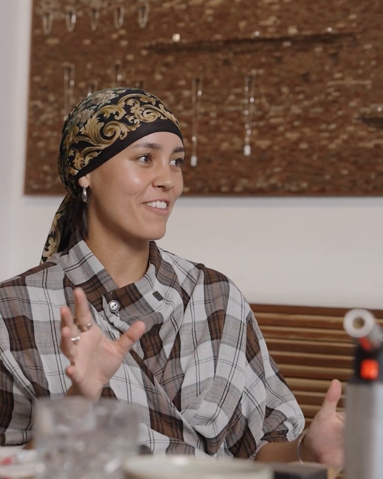 Person sitting at a table with tools and equipment, wearing a plaid shirt and headband.
